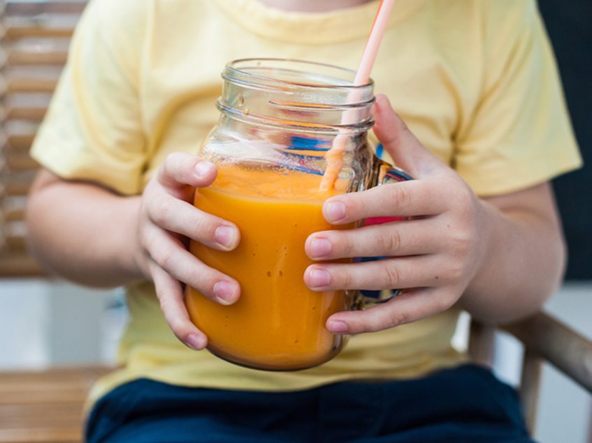 Child holding orange juice in mason jar 