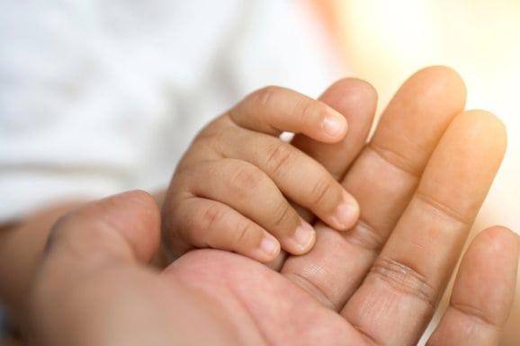 Closeup on a baby's hand holding a parent's hand